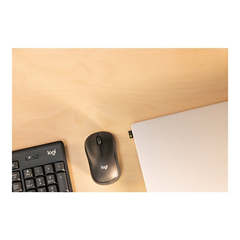 Draufsicht auf einen Schreibtisch. Darauf liegen eine schwarze Tastatur und Maus der Marke Logi, ein Laptop und ein Empfänger.