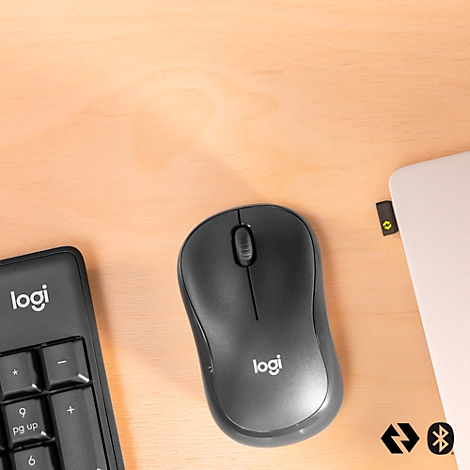Wireless mouse and number pad by Logitech on light brown wood. A laptop is visible on the right edge.