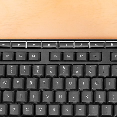 Overhead view of a black keyboard on a wooden surface. Letters, numbers and special characters are clearly visible.