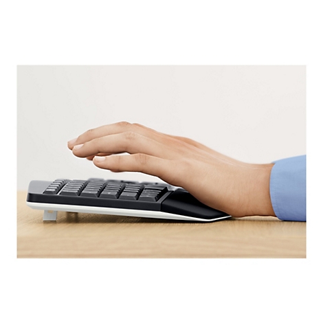 Mains tapant sur un clavier noir avec un repose-paume. En arrière-plan, un champ clair et homogène et une surface en bois.