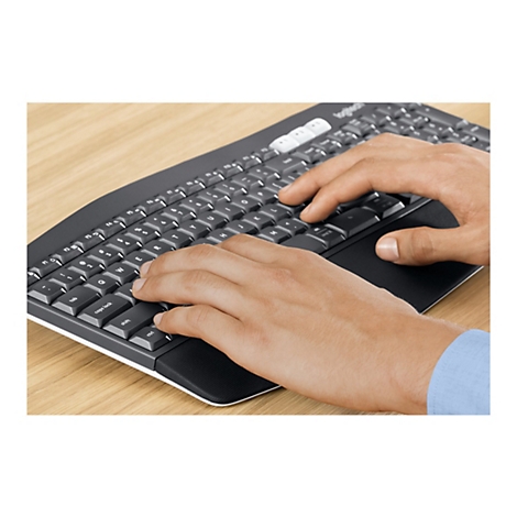Gros plan d'une personne tapant sur un clavier Logitech sombre ; mains sur les touches, manche bleu en arrière-plan.