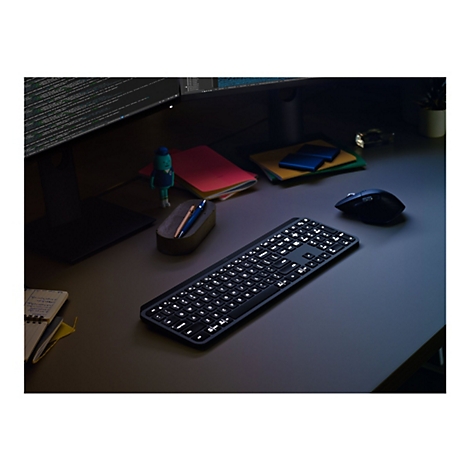 Draufsicht auf eine beleuchtete schwarze Tastatur auf einem Schreibtisch. Neben der Tastatur liegen eine Maus, Notizbücher und dekorative Gegenstände.