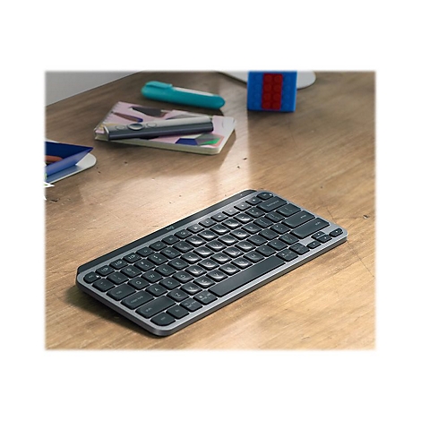 Drahtlose, dunkle Tastatur auf einem Holzschreibtisch. Im Hintergrund Notizbuch und Stifte.