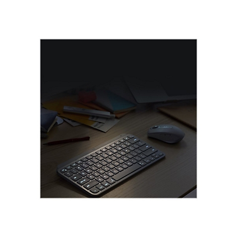 Eine beleuchtete Tastatur und Maus auf einem Holztisch. Im Hintergrund Notizen und ein Laptop.