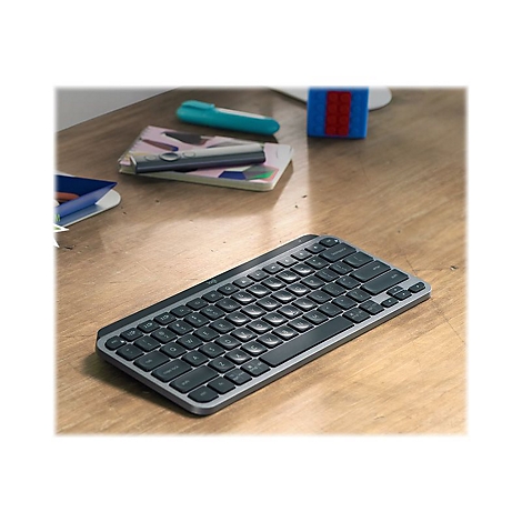 Drahtlose Tastatur auf einem Holztisch mit Notizbuch, Stift und Spielzeug im Hintergrund.