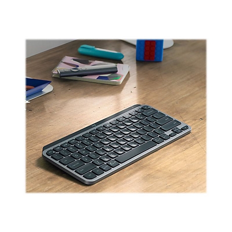 Draufsicht auf eine graue Tastatur mit schwarzen Tasten auf einem Holztisch. Im Hintergrund liegen weitere Gegenstände.