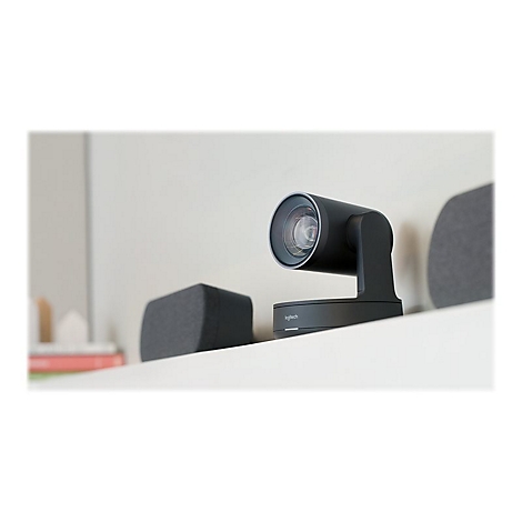 Schwarze Logitech-Webcam auf einer weißen Ablage. Im Hintergrund: Graue Lautsprecherboxen und ein Buch.