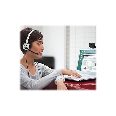 Eine Frau mit Headset vor Laptop, tippt, spricht. Webcam oben. Auf dem Bildschirm: Webseite.