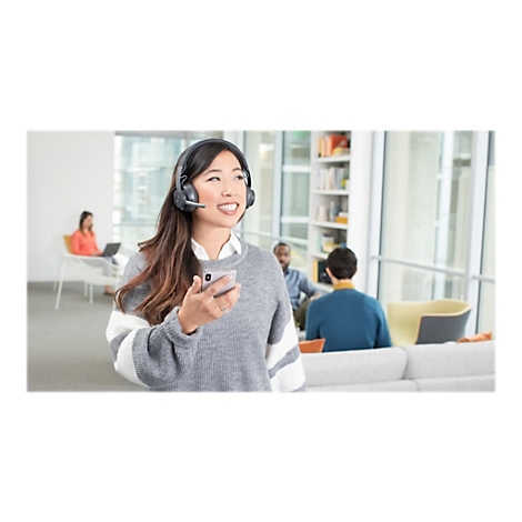 Une femme souriante avec un casque et un smartphone dans un bureau, d'autres employÃ©s en arriÃ¨re-plan.