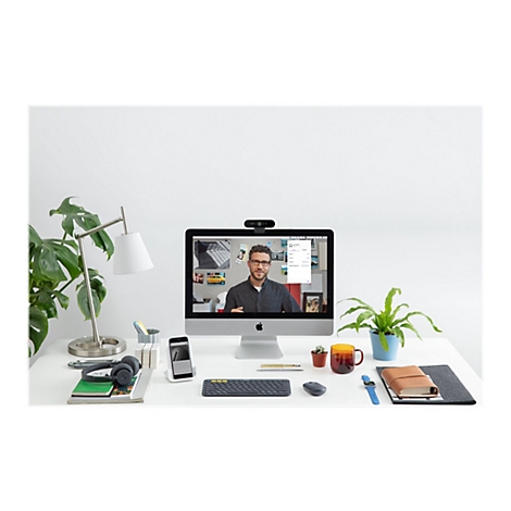 Un espace de travail avec un Ã©cran affichant une visioconfÃ©rence. Des plantes, des cahiers, des stylos, un casque et une webcam sont sur la table.
