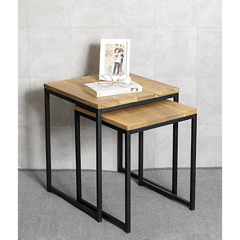 Deux tables carrées en bois avec des cadres métalliques sont empilées l'une sur l'autre. Sur la table du dessus se trouvent un livre, des lunettes et un cadre photo.