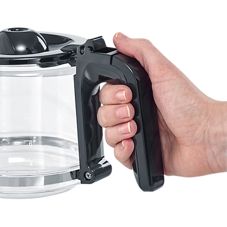 Gros plan : une main tient la poignée noire d'une cafetière en verre. Les doigts et la carafe sont clairement visibles.