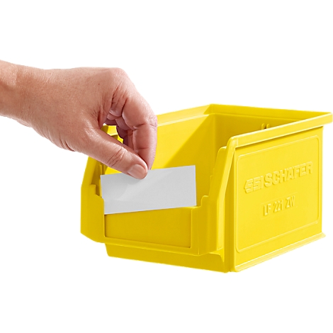Een hand plaatst een wit label in de houder van een gele opslagbak van SSI Schäfer.
