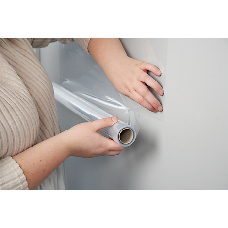 Hände halten eine Rolle transparente Folie, die an einer grauen Wand befestigt wird.