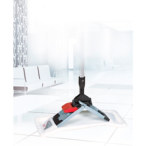 Grey mop with red lever stands on a light tiled floor. In the background, a bright waiting area with white furniture.