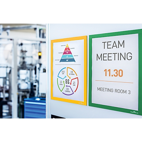 Two boards on the wall. Left: yellow framed infographic with diagrams. Right: green board with Team Meeting, 11.30, Room 3.