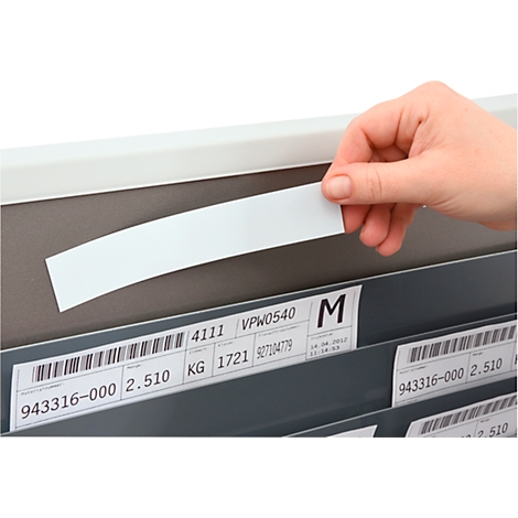 Hand holding a white sticker over labels in a shelf.