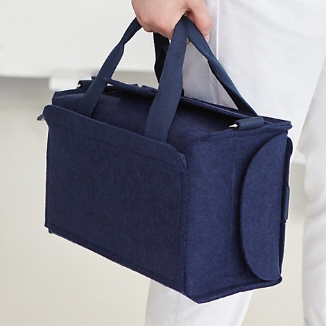 Eine dunkelblaue Filztasche wird per Schlaufe flexibel am Griff eines schwarzen Rollkoffers befestigt.