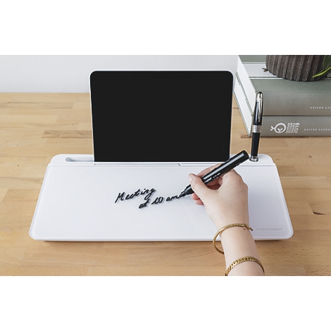 Eine Hand schreibt mit einem Stift auf ein weißes Desktop-Whiteboard, hinter dem ein Tablet steht.