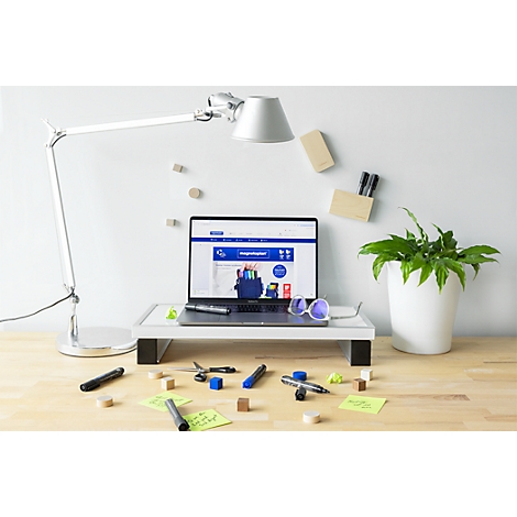 Laptop auf einem Monitorständer auf einem Schreibtisch mit Schreibtischlampe, Pflanze und verstreutem Büromaterial.
