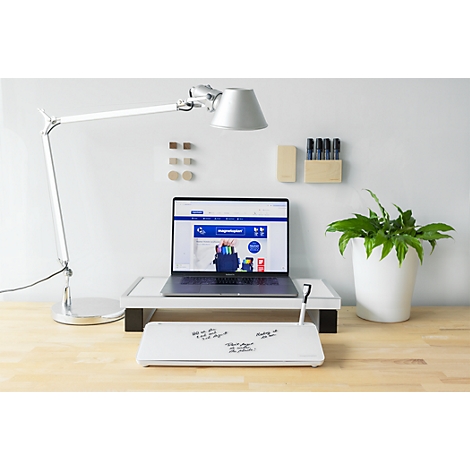 Ein moderner Schreibtisch mit Laptop auf einem Ständer, einer Schreibtischlampe, einer Pflanze und einer Notiztafel.