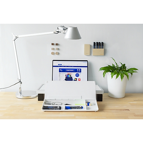 Aufgeräumter Schreibtisch mit weißem Organizer, Lampe, Laptop und Pflanze vor einer hellen Wand.