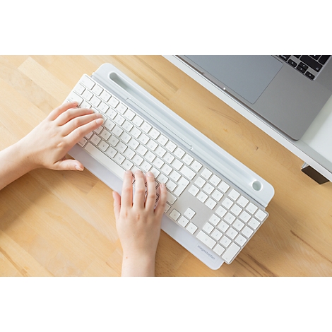 Hände tippen auf einer weißen Tastatur mit integrierter Halterung auf einem hellen Holztisch.