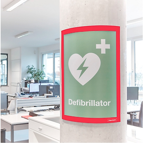Ein grünes Defibrillator-Schild an einer Betonsäule in einem hellen Büro.