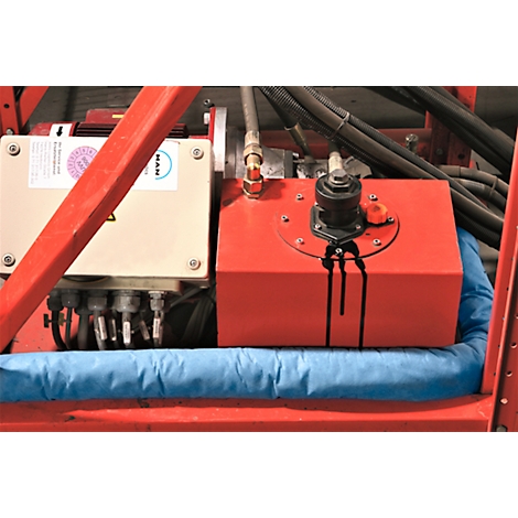 Piezas de máquina: contenedor rojo con aceite derramado, junto a una caja gris. Cojín azul debajo del contenedor, marcos rojos.