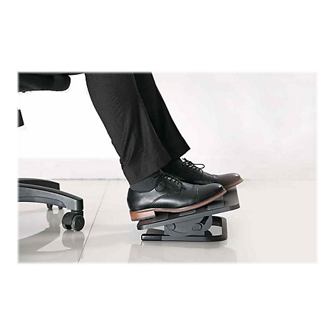 Beine eines Mannes mit schwarzen Schuhen auf einer FuÃŸstÃ¼tze. Im Hintergrund ein BÃ¼rostuhl.