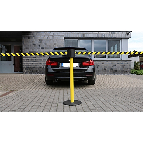 A black car is parked behind a yellow barrier with black and yellow stripes.