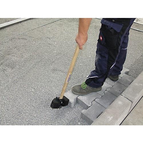 Un ouvrier pose des pavés avec un marteau. Il se tient sur les pierres, tient le marteau et les frappe.