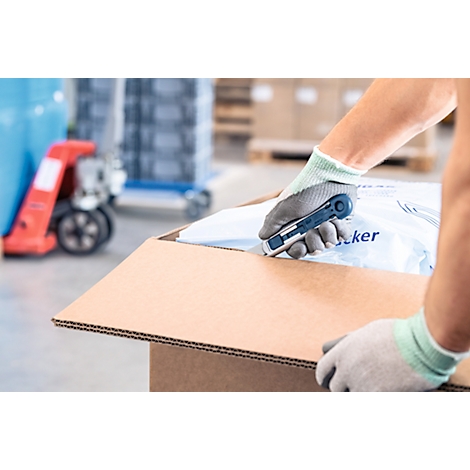 Person schneidet Karton mit Messer. Hände mit Handschuhen, im Hintergrund Warenlager.