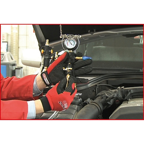 Mechaniker in roter Jacke und Handschuhen misst den Druck in einem Motorraum mit einem Messgerät.