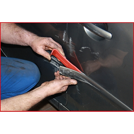 Nahaufnahme von Händen, die mit einem roten Werkzeug einen schwarzen Streifen an einer Autotür befestigen.