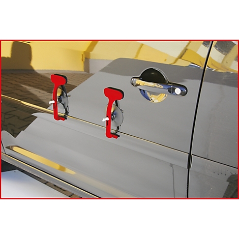 Rote Ausbeulwerkzeuge an Autotür. Im Hintergrund die gelbe Fassade eines Gebäudes.