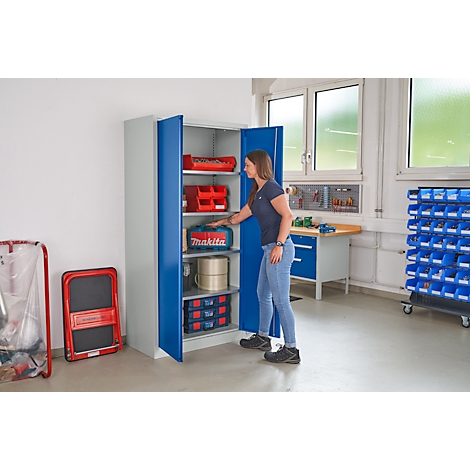 Een vrouw opent een blauwe kast in een werkplaats. Binnenin staan gereedschapskisten en accessoires.