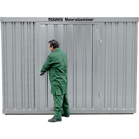 A man in green workwear opens the door of a gray material container. The container has the lettering "FLADAFI Materialcontainer".