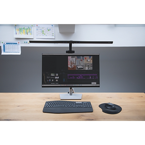 Bureau avec moniteur, clavier, souris et éclairage d'écran. Un programme de montage vidéo est ouvert sur le moniteur, des notes sont accrochées au mur.