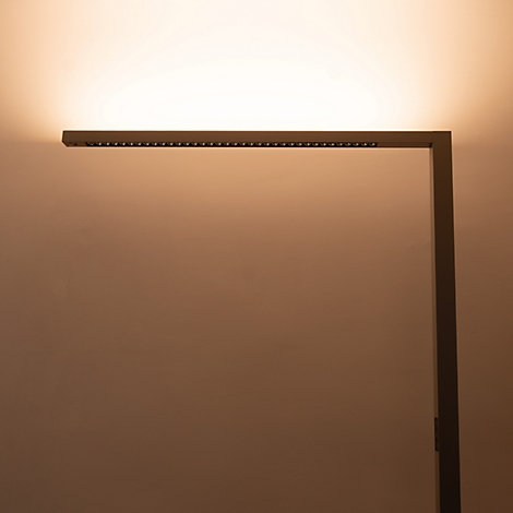 Eine minimalistische, dunkle LED-Stehleuchte wirft warmes, indirektes Licht an die Wand.