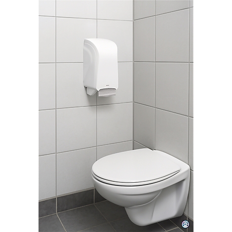 Distributeur de serviettes en papier blanc au-dessus de toilettes murales. Mur carrelé, sol gris.