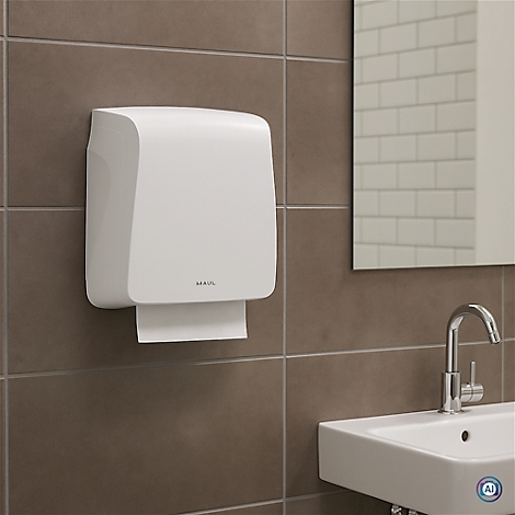 Weißer Papierhandtuchspender an brauner Wand. Spiegel, Waschbecken und Wasserhahn im Hintergrund.