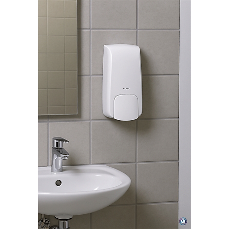 Witte zeepdispenser aan een lichtgrijze betegelde muur. Daaronder een wastafel met een chromen kraan.