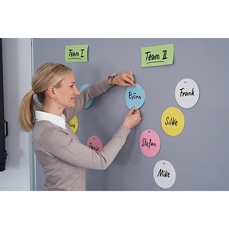 A woman is arranging name tags on a wall. The wall has the inscriptions 'Team I' and 'Team II'.