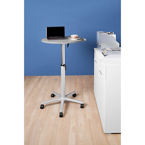 A height-adjustable standing desk with a laptop and a coffee cup. Against a blue background and light wooden floor.