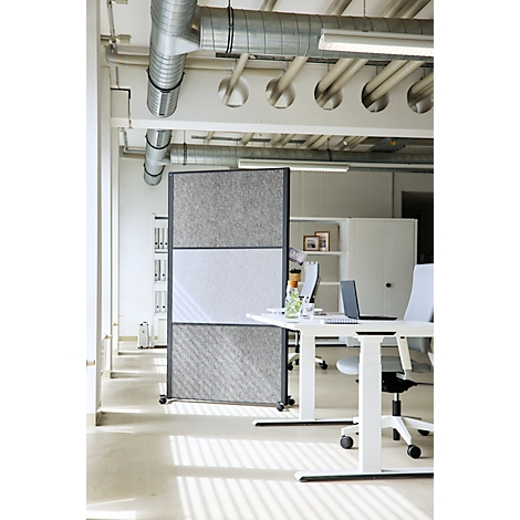 Ein mobiler grauer Trennwand-Paravent in einem modernen, hellen Loft-Büro mit Industriedesign.