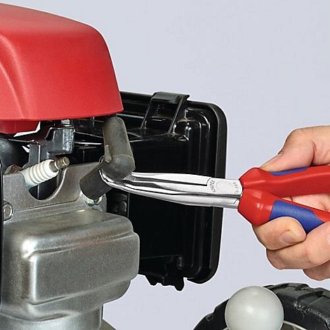 Een hand houdt een rode en blauwe tang vast om een bougiedop op een motor te verwijderen.