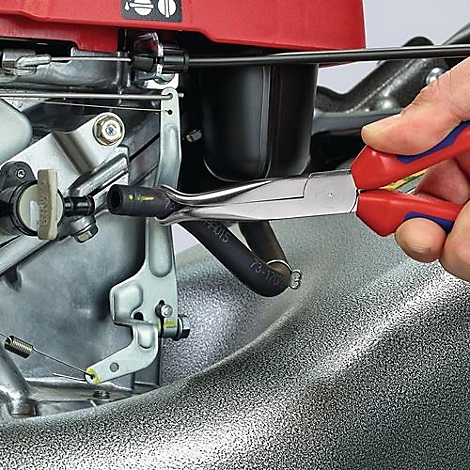 Een hand houdt een tang vast om een slang aan een grasmaaier te bevestigen. Close-up.