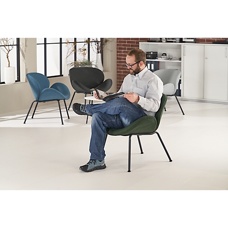 Ein Mann in Jeans und Hemd sitzt in einem grünen Sessel und liest. Im Hintergrund weitere Stühle und ein Fenster.