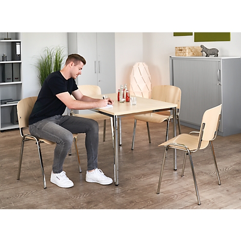 A man is sitting at a table writing. There are drinks on the table and chairs next to it.